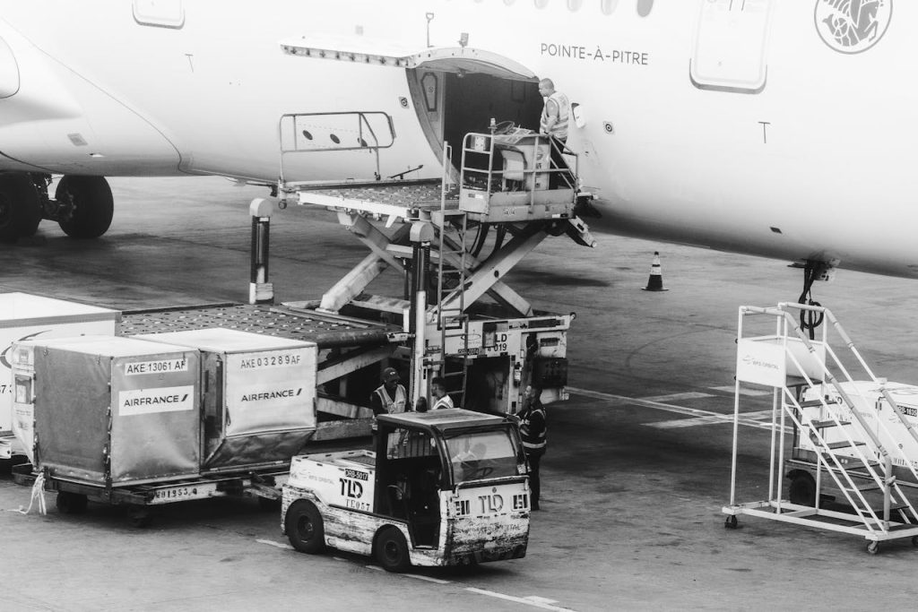 Black and white image of cargo being loaded on an airplane at an airport.